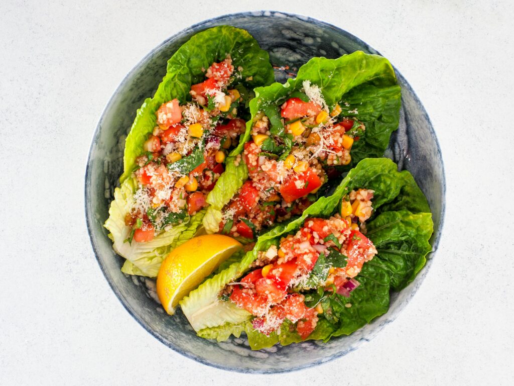 A vibrant vegetable salad with romaine lettuce, tomatoes, and corn served in a stoneware bowl with a lemon wedge.