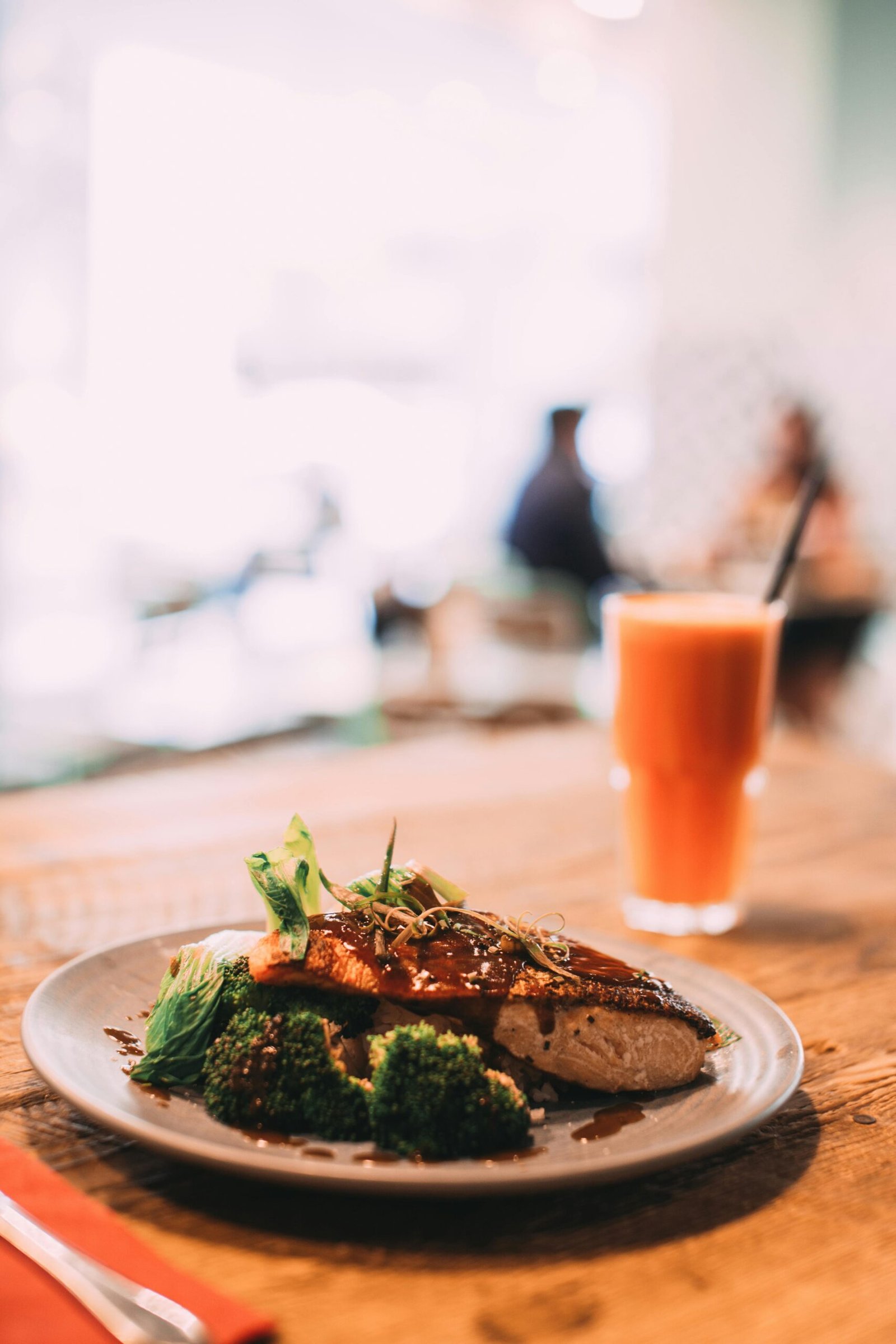 A tantalizing salmon dish served with broccoli and carrot juice on a wooden table in a restaurant setting.