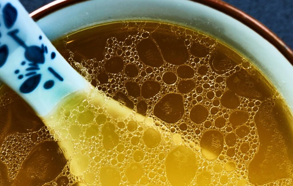 Warm, comforting chicken broth in a bowl with decorative spoon close-up.