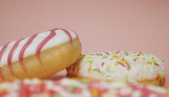 Close-up of delicious donuts with colorful icing and sprinkles on a pink background.