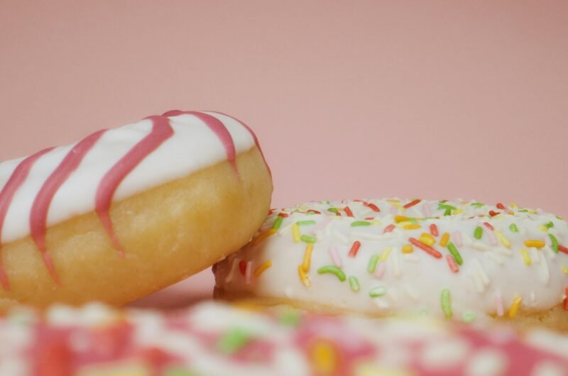 Close-up of delicious donuts with colorful icing and sprinkles on a pink background.