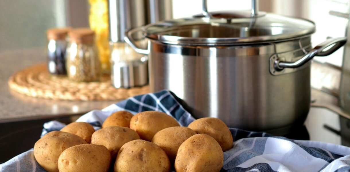 Fresh potatoes on cloth beside a stainless pot, ready for cooking in a modern kitchen.