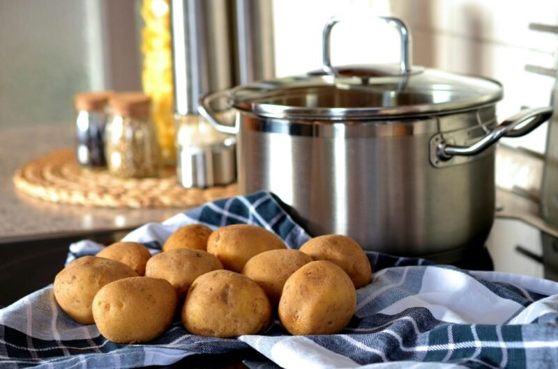 Fresh potatoes on cloth beside a stainless pot, ready for cooking in a modern kitchen.