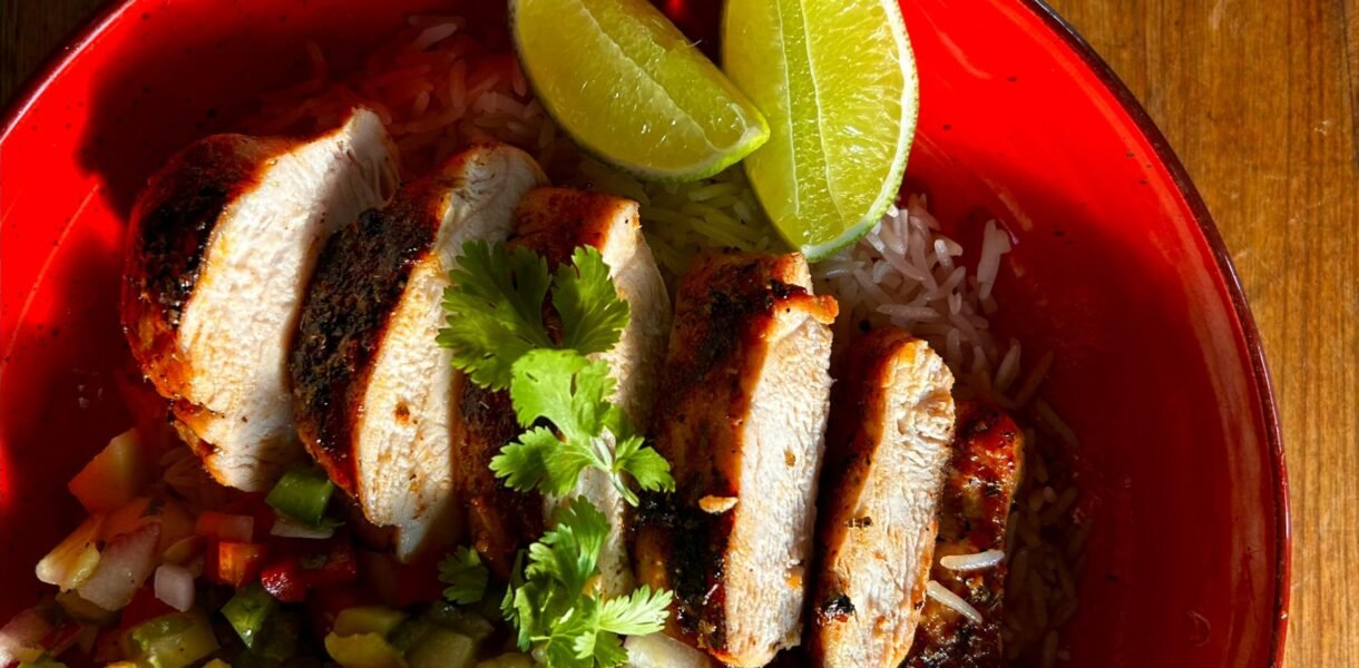 Grilled chicken with fresh salsa and lime slices served on a red plate. Perfect for a vibrant meal.