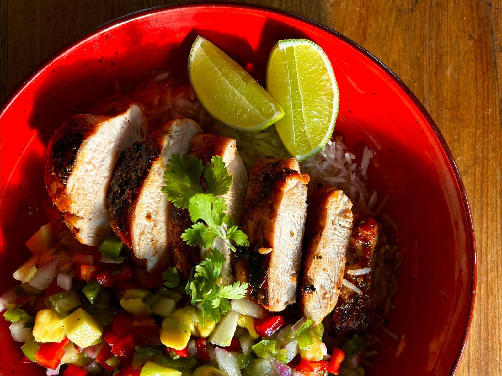 Grilled chicken with fresh salsa and lime slices served on a red plate. Perfect for a vibrant meal.