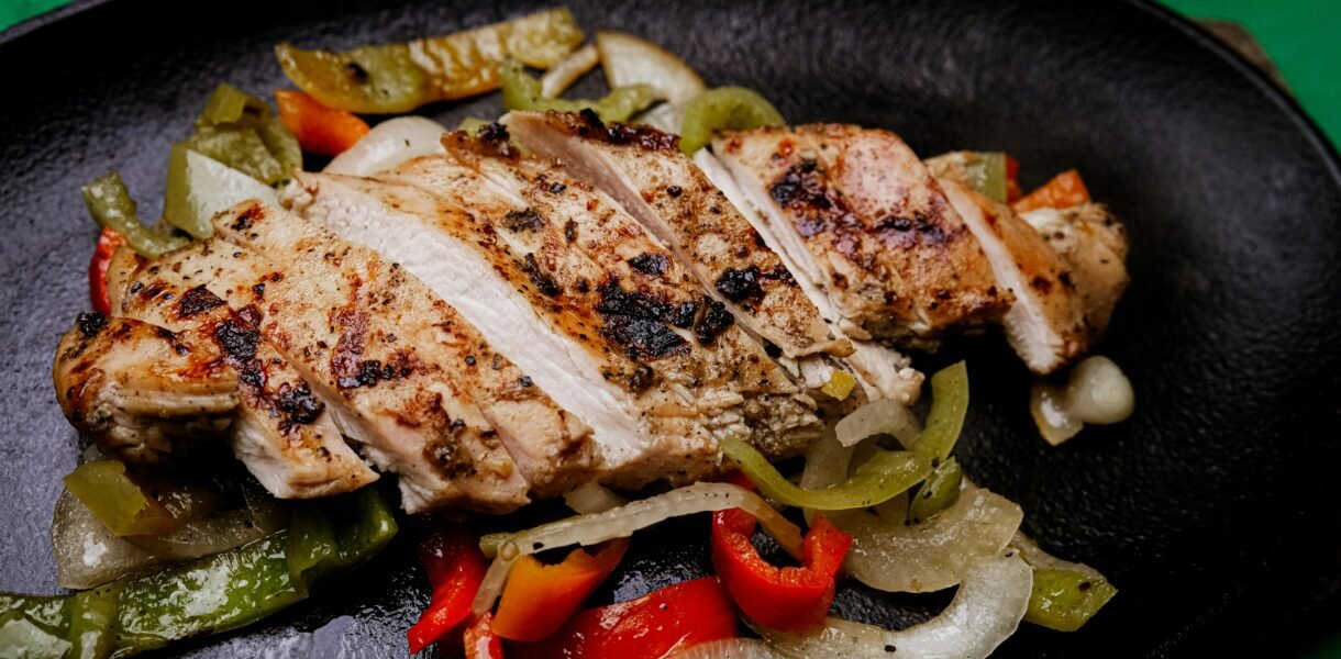 Succulent grilled chicken with vibrant peppers on a sizzling plate, perfect for a tasty meal.