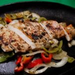Succulent grilled chicken with vibrant peppers on a sizzling plate, perfect for a tasty meal.