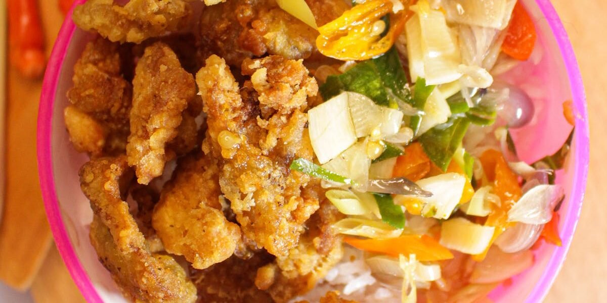 Indonesian crispy fried chicken served with salad on a wooden board.