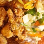 Indonesian crispy fried chicken served with salad on a wooden board.